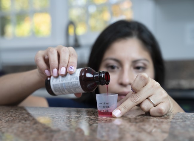 Hispanic/Latinx woman with dark hair measuring liquid medicine